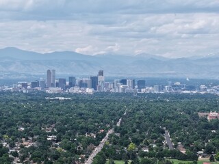 Panoramic drone shot: beautiful Denver metropolitan area, lush green urban forest, and dramatic mountain backdrop. Travel and landscape