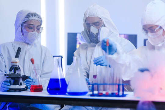 A team of chemists in hazmat suits discusses a breakthrough during a critical experiment in a secure lab. Concept for drug discovery and chemical research.