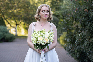 Elegant bride in a white tea-length wedding dress holding a bouquet of ivory and blush roses with...