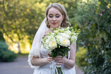 Bride in a white wedding dress holding an elegant bouquet of ivory and blush roses with green buds,...