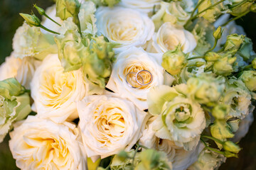 Elegant wedding bouquet of soft ivory and pastel peach roses with delicate green buds. Two gold...
