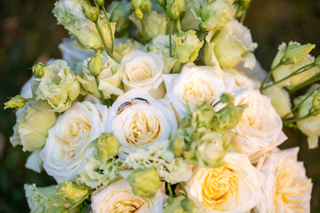 Elegant wedding bouquet of soft ivory and pastel peach roses with delicate green buds. Two gold wedding rings rest on the center rose, symbolizing love and commitment. Perfect for wedding invitations