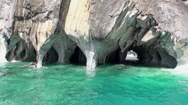 Watercraft is shown navigating through the naturally sculpted Marble Caves. Observe the mesmerizing reflections in the bright turquoise water during daylight hours on Lago General Carrera.