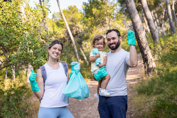 Happy family posing with full trash bag after forest cleanup