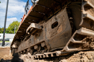 View of tracked excavator undercarriage on construction site showing detailed steel track links and heavy-duty machinery movement on dirt terrain during groundwork operations