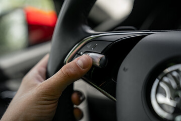 Driver hand operating multifunction steering wheel button in modern car interior with integrated...