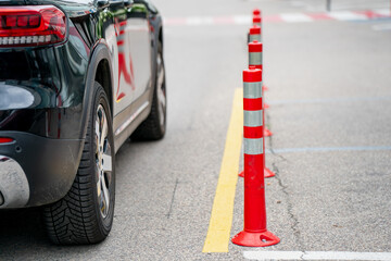 Car parked near row of red reflective traffic cones on asphalt road with yellow line for safety and...