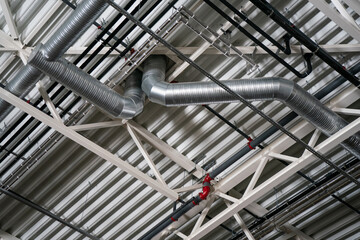 Modern industrial ceiling with metal air ventilation ducts, cable trays and fire sprinkler system installed in warehouse or factory construction interior with steel roof structure