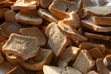 A close-up shot of a pile of rustic, toasted bread slices, showcasing their varied textures and golden-brown hues. The bread appears homemade, possibly slightly coarse, hinting at a wholesome
