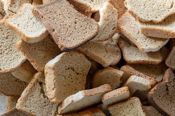 A close-up shot of a pile of rustic, toasted bread slices, showcasing their varied textures and golden-brown hues. The bread appears homemade, possibly slightly coarse, hinting at a wholesome