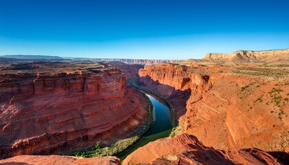 majestic canyon landscape with layered red rock cliffs and deep winding river under clear blue sky in a vast arid desert environment
