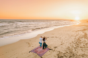 Couple practicing yoga on the beach at sunset