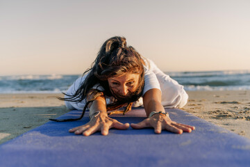 Focused woman stretching on beach yoga mat at sunrise