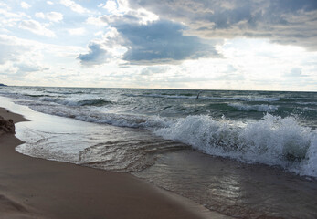 Powerful lake waves crashing on a sandy beach under cloudy sky