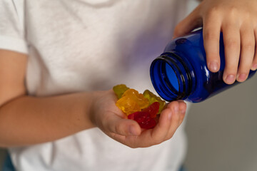 Kid hand hold a bottle from which colorful vitamins in the shape of jelly bears have poured out. Multivitamins or jelly candies for children. Vitamins for children.