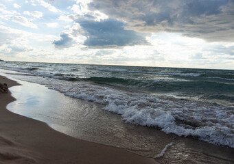 Powerful lake waves crashing on a sandy beach under cloudy sky