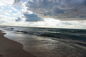 Gentle waves on sandy beach with dramatic clouds above