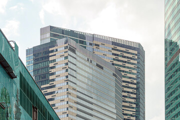 A modern high-rise building with a mirrored facade rises against a clear sky. The structure’s geometry and reflections emphasize style and urban aesthetics.