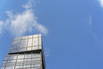 The top part of the skyscraper with mirrored windows reflects the blue sky and clouds, creating a shimmering and airy effect.