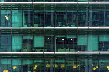 The office building facade with glass windows offers a glimpse into interior workspaces and equipment. 