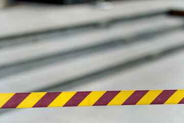 A caution tape with bright yellow diagonal stripes is stretched in front of stairs, indicating a potentially hazardous or restricted area. 