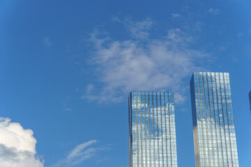 Two glass skyscrapers rise against the blue sky, reflecting clouds and creating a sense of...