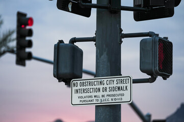 Traffic signal pole with pedestrian crossing buttons and warning sign prohibiting obstruction,...