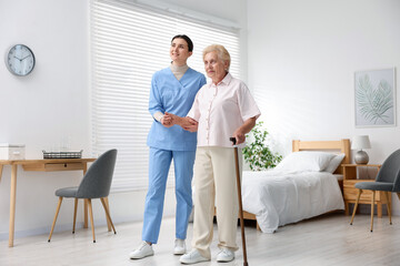 Nurse assisting senior woman with walking cane indoors. Home health care service