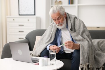 Senior man with thermometer having online consultation with doctor via laptop at home
