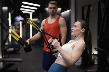 Fototapeta premium Young woman exercising with suspension trainers with professional personal coach in gym