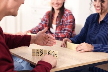 Friends playing dominoes at light wooden table indoors, closeup