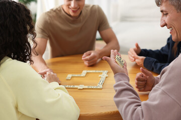 Friends playing dominoes at wooden table indoors, closeup