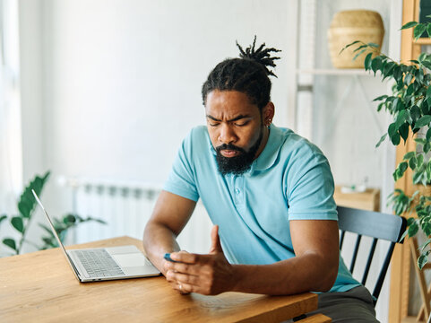 Portrait of a young black man chatting with girlfriend at home, using modern mobile phone, checking social media, using mobile app, texting or browsing internet on his phone