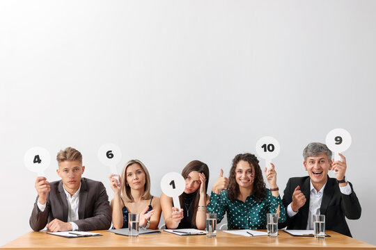 Panel of judges voting with score signs at table against light grey background