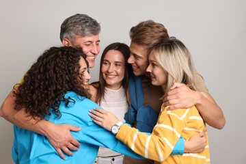 Group of happy friends hugging on grey background
