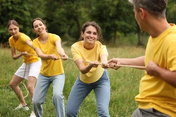 Fototapeta premium Team building. Group of happy people playing tug of war with rope outdoors