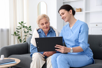 Nurse with clipboard examining senior woman indoors. Home health care service