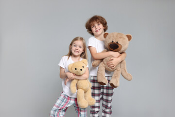 Cute little children in pajamas with teddy bears on grey background