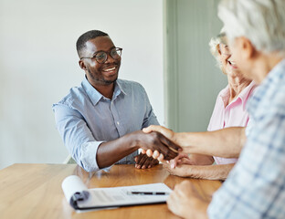 Portrait of a businessman or real estate agent shaking hands with senior couple in his office