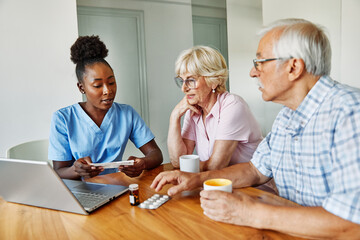 Doctor or nurse caregiver showing a prescrption or documents and holding drug bottle to senior couple man and woman at home or nursing home
