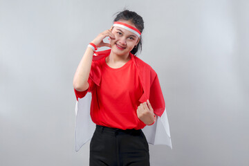 Cheerful Indonesian girl smiling and making hand-heart gesture, celebrating Independence Day in red and white outfit with pride and love.