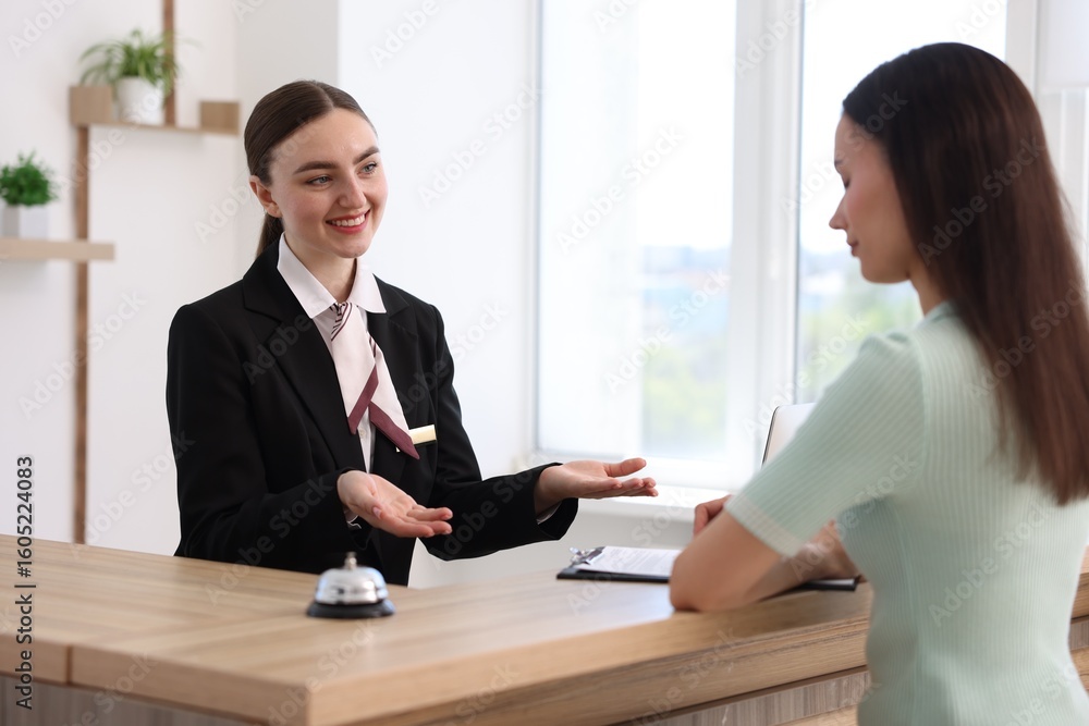 Poster smiling receptionist working with guest at reception desk indoors