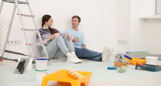 Couple with cups of coffee having break during renovation at home - Powered by Adobe