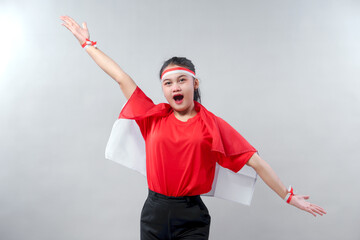 Energetic young Indonesian woman raises her arms joyfully while wearing red and white outfit....