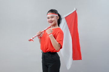 Confident young woman in red shirt proudly holding Indonesian flag on her shoulder, smiling and...