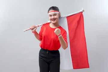 Energetic young woman smiling and holding Indonesian flag with pride, showing a victory fist on...