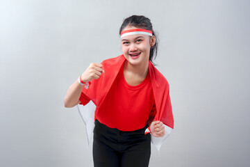 Young Indonesian woman in red shirt smiling and raising her fist with national flag on shoulders,...