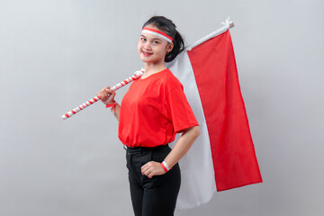 Proud young woman in red shirt confidently holding Indonesian flag on her shoulder, smiling calmly...