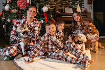 Hispanic family with pets wearing Christmas pajamas by decorated tree