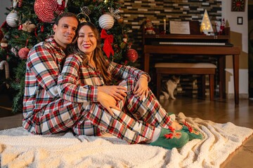 Couple in pajamas hugging in front of Christmas tree at home